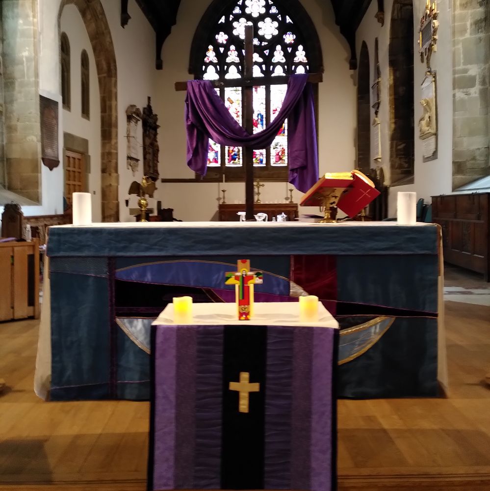 A small children's altar in front of the nave altar both dfressed in purple with a large wooden cross behind