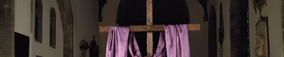 A large wooden cross with a purple cloth draped over it and candles either side