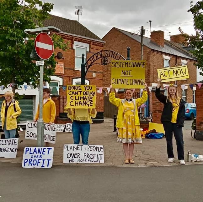 a crowd of protestors outside of the mp for Loughborough's office. They are dressed in yello and holding placards with messages about the need to act to stop the climate emergency.