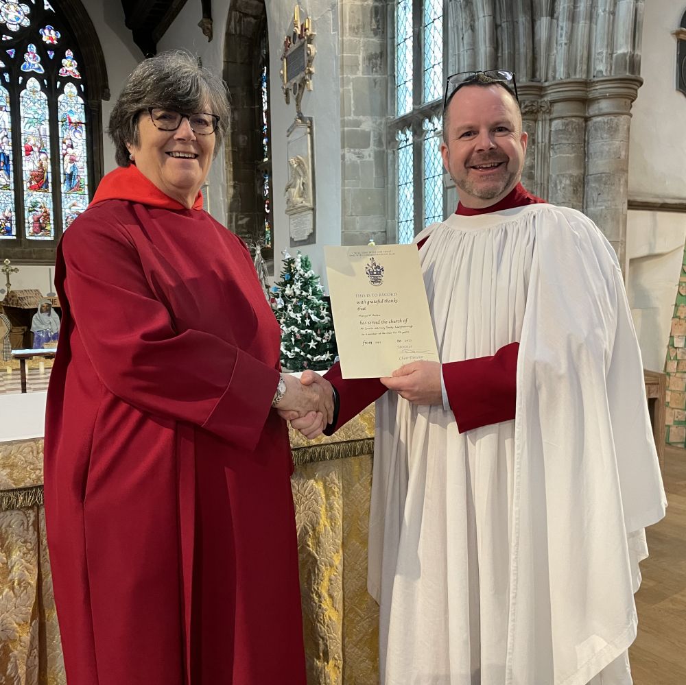 Margaret Bates pictured receiving a certificate for 25 years long service from choir director SImon Headley. Both are dressed in their formal choir robes.