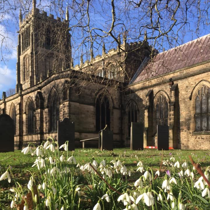 A close up of snowdrops in the grounds outside the church with te church building in the background