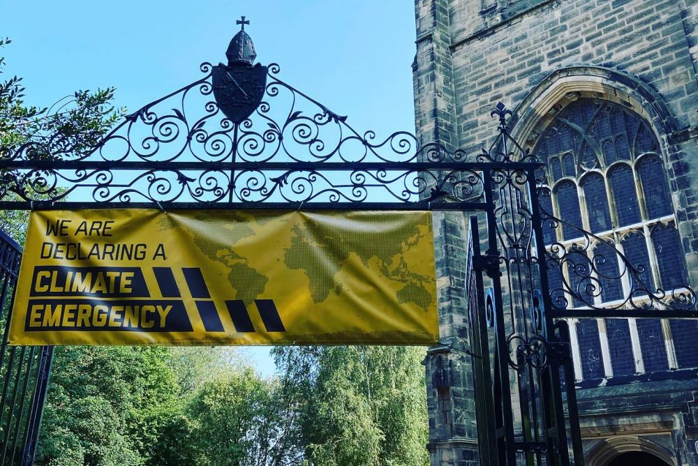 A yellow banner declaring a climate emergency attached to the iron gates of All saints with Holy Trinity Church Loughborough