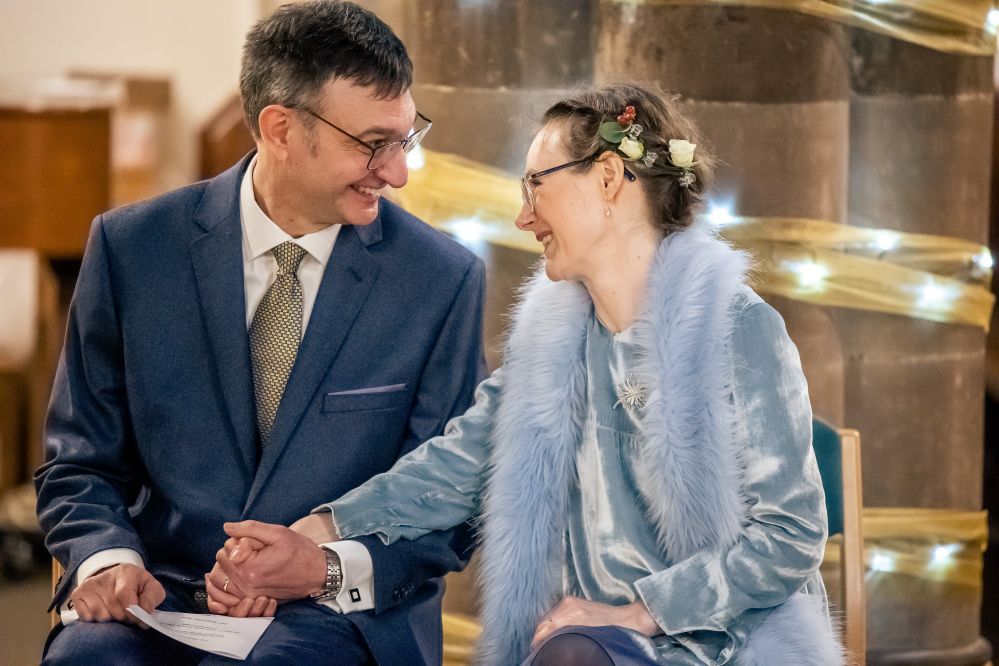 A bride and groom staring at each other lovingly in a church whilst holding hands.