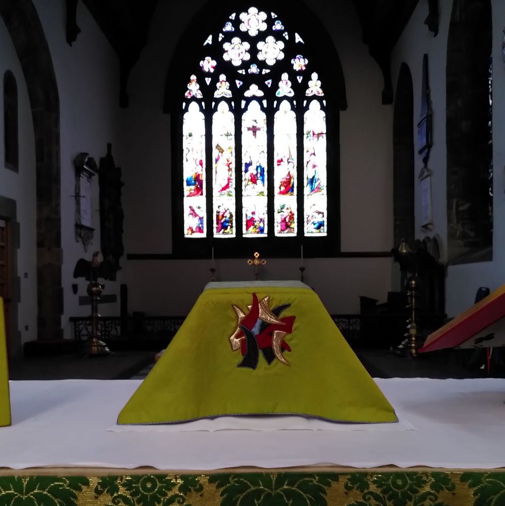 The altar table in the church set with the communion vessels with a large stained glass window in the background