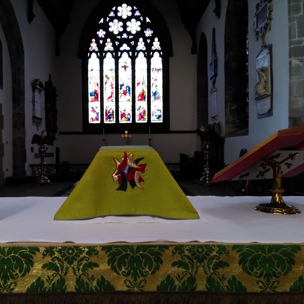 The altar table in the church set with the communion vessels with a large stained glass window in the background