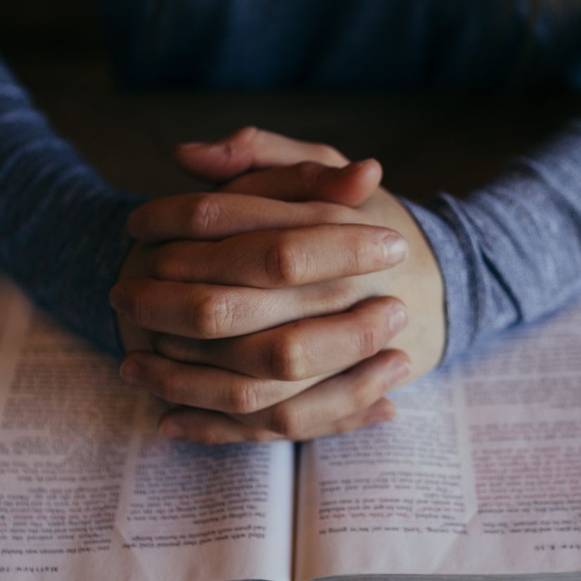A pair of hands clasped together in prayer on top of a bible.