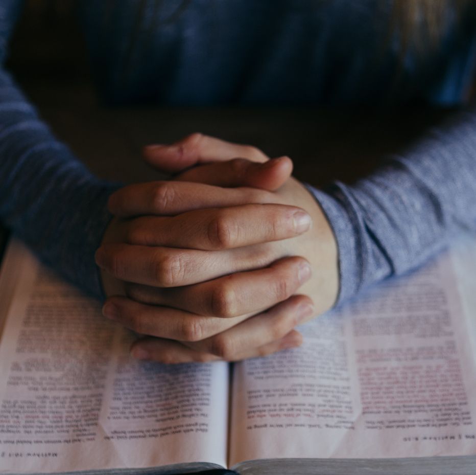 A pair of mens hands clasped together in prayer on top of a bible