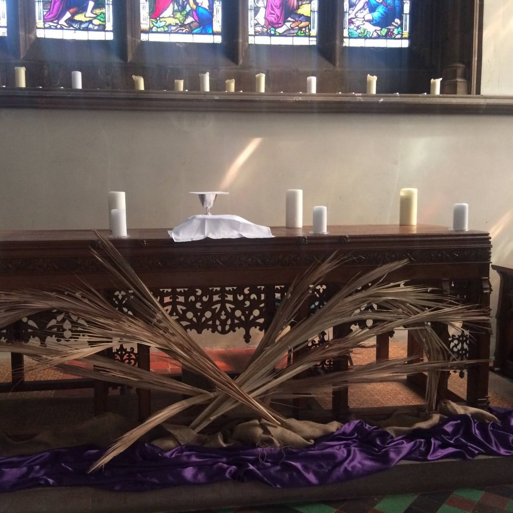 The reserved sacrament on a wodden alter surrounded by candles and palm leaves. A shat of sunlight is shining on to the chalice.