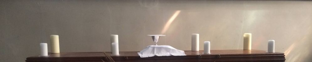 The reserved sacrament on a wodden alter surrounded by candles and palm leaves. A shat of sunlight is shining on to the chalice.