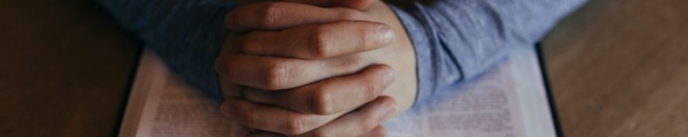 Hands clasped in prayer over a bible