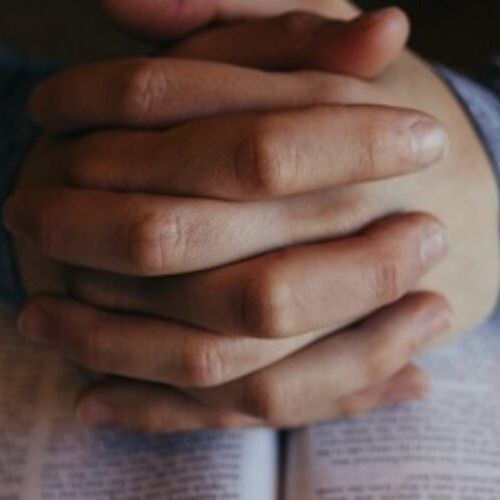 Hands clasped in prayer over a bible