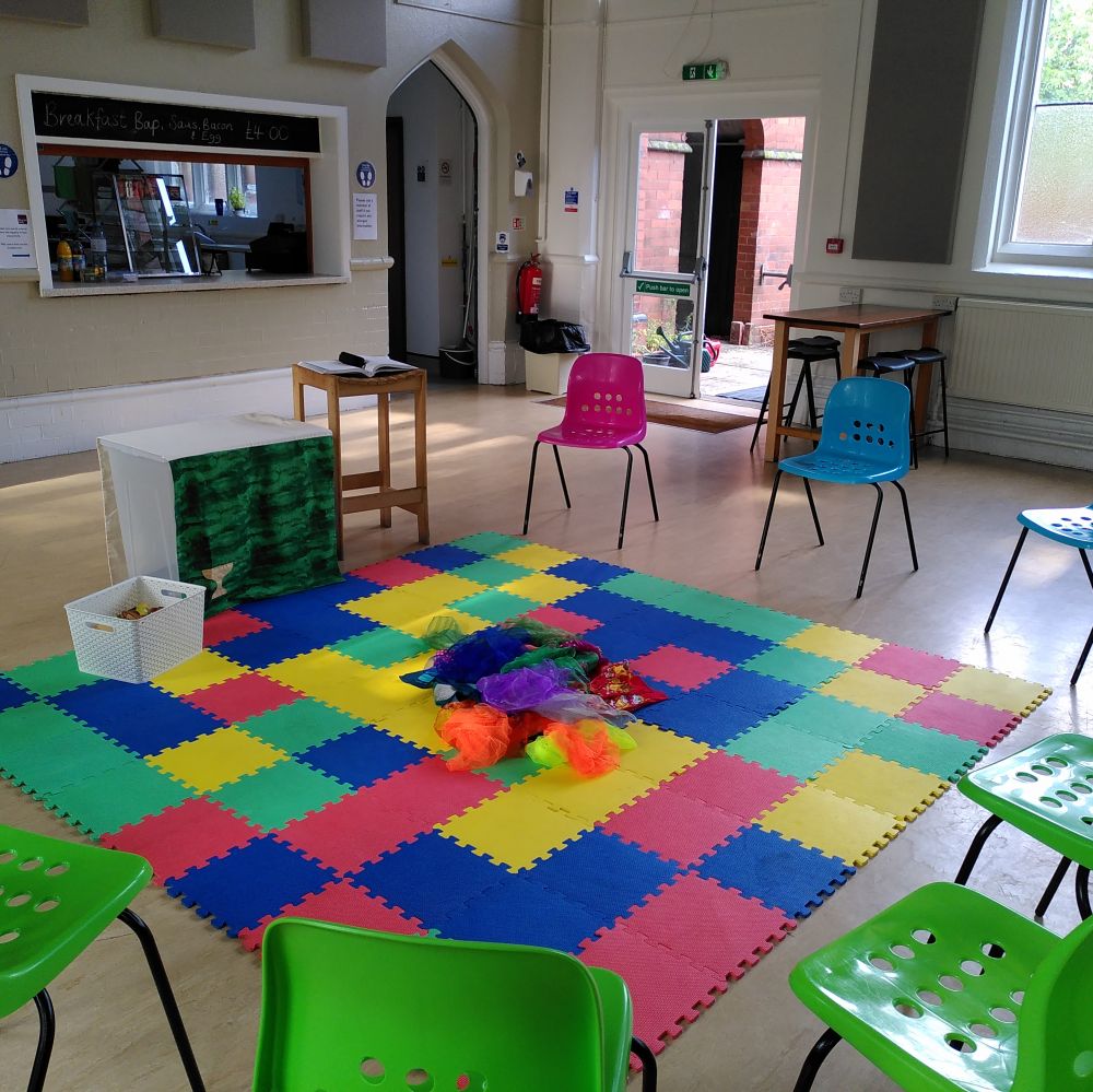 A circle of chairs around some colourful mats for children with a small altar table