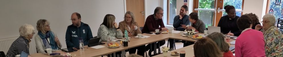 A group of people sitting around a table at a meeting engaged in conversation with each other